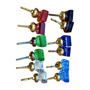 May include: A collection of colorful glass cabinet knobs. The knobs feature square or rectangular glass in shades of red, green, blue, and clear. Each knob has a brass-colored base and a threaded screw for installation.