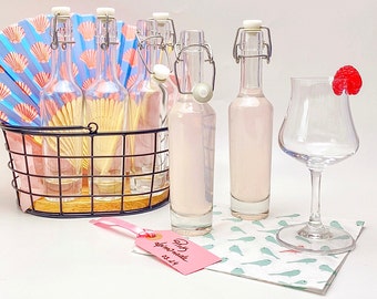 May include: A set of six clear glass bottles with silver lids filled with a pink liquid. The bottles are in a wire basket with a pink and blue fan behind them. A pink tag with the text "Mit Liebe gemacht 03.2019" is in the foreground.