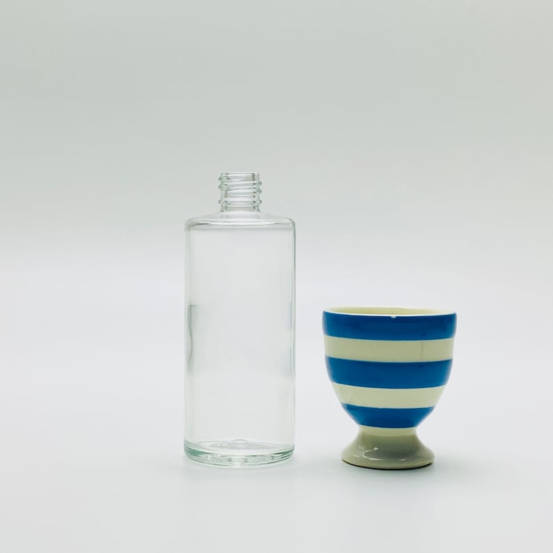 May include: A clear glass bottle with a white and blue striped ceramic egg cup.