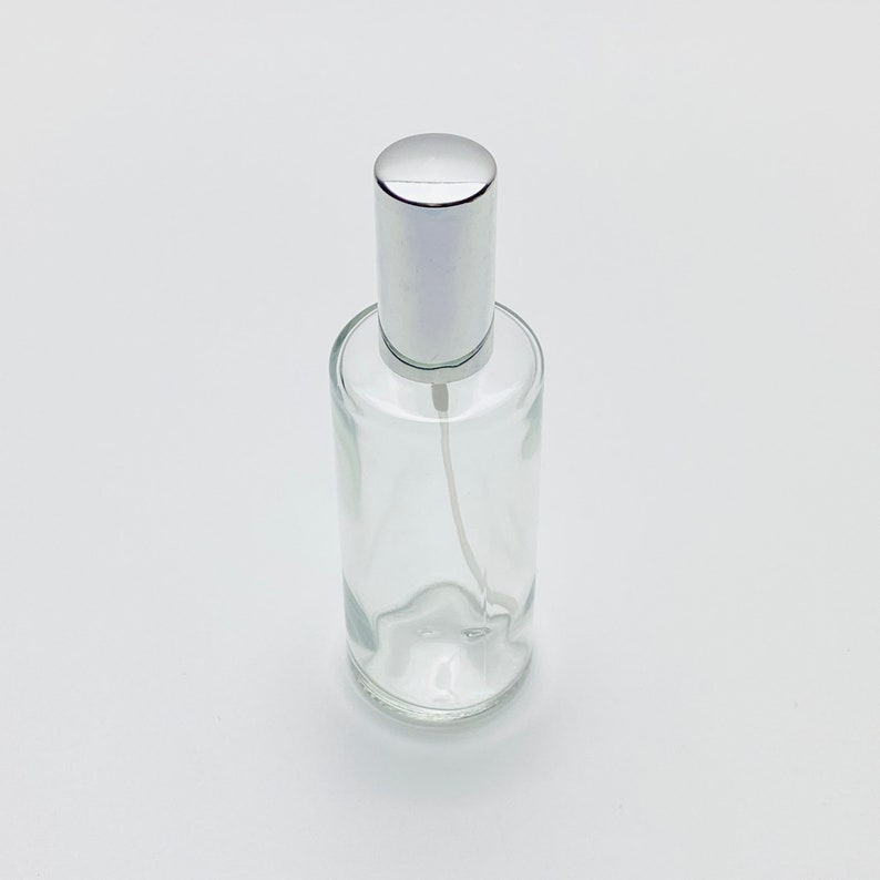 May include: A clear glass bottle with a silver spray top. The bottle is empty and ready to be filled.
