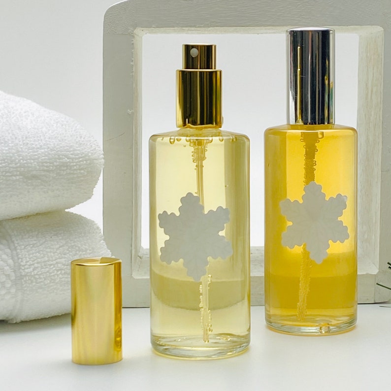May include: Two clear glass bottles with gold and silver spray tops. Both bottles contain a yellow liquid and have a white snowflake sticker on the front.