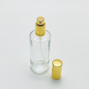 May include: A clear glass bottle with a gold spray top and a separate gold cap. The bottle is empty and ready to be filled.