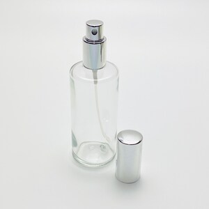 May include: A clear glass bottle with a silver spray top and a silver cap. The bottle is empty and ready to be filled.