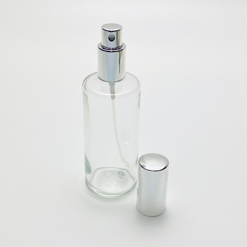 May include: A clear glass bottle with a silver spray top and a silver cap. The bottle is empty and ready to be filled.