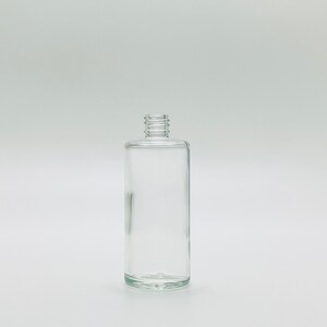 May include: A clear glass bottle with a cylindrical shape and a simple design. The bottle has a smooth, polished surface and a rounded bottom.
