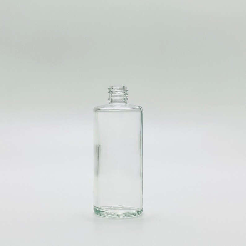 May include: A clear glass bottle with a cylindrical shape and a simple design. The bottle has a smooth, polished surface and a rounded bottom.