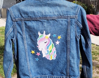 May include: A blue denim jacket with a colorful unicorn and stars embroidered on the back.