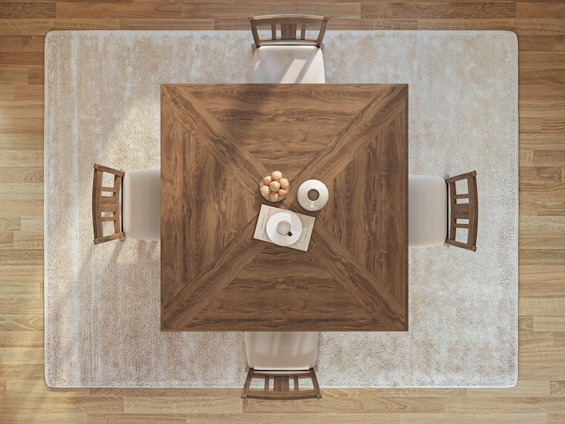 Puede incluir: Una mesa de comedor cuadrada de madera con un acabado marr&oacute;n claro y una alfombra blanca debajo. Cuatro sillas rodean la mesa, cada una con un marco de madera marr&oacute;n claro y un coj&iacute;n blanco. Un plato blanco con una taza y un platillo se encuentra sobre la mesa, junto con un peque&ntilde;o cuenco de fruta.