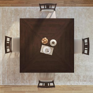 Puede incluir: Una mesa de comedor cuadrada de color marr&oacute;n oscuro con cuatro sillas. La mesa est&aacute; puesta con un cuenco de fruta, una taza y un platillo, y un objeto decorativo. La mesa est&aacute; sobre una alfombra blanca.