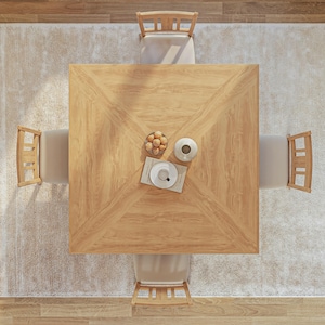 Puede incluir: Una mesa de comedor cuadrada de madera con cuatro sillas, colocada sobre una alfombra beige claro. La mesa tiene un patr&oacute;n de veta de madera clara y est&aacute; rodeada de cuatro sillas con marcos de madera clara y cojines beige. Un taz&oacute;n de fruta y un jarr&oacute;n con una flor est&aacute;n sobre la mesa.