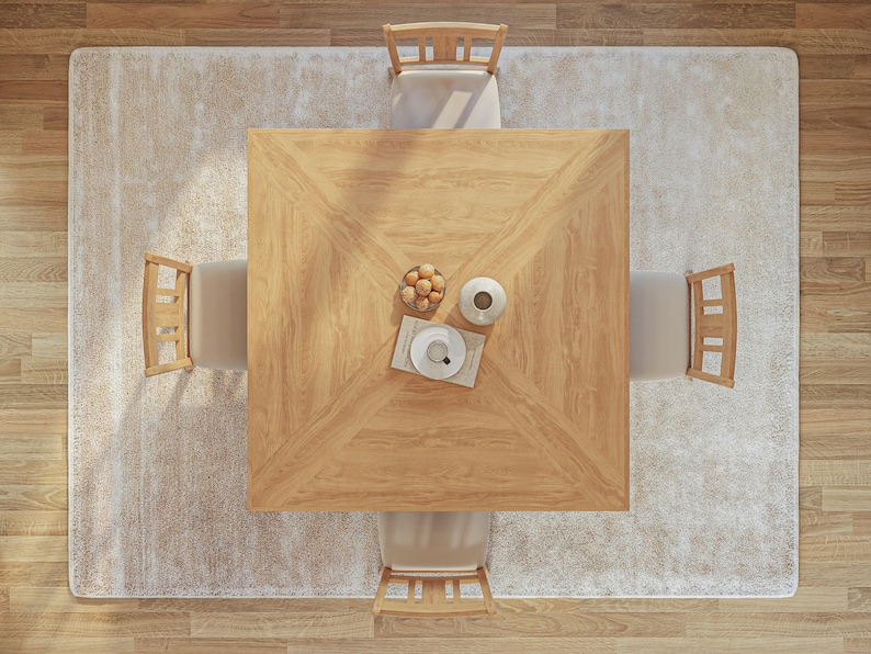 Puede incluir: Una mesa de comedor cuadrada de madera con cuatro sillas, colocada sobre una alfombra beige claro. La mesa tiene un patr&oacute;n de veta de madera clara y est&aacute; rodeada de cuatro sillas con marcos de madera clara y cojines beige. Un taz&oacute;n de fruta y un jarr&oacute;n con una flor est&aacute;n sobre la mesa.
