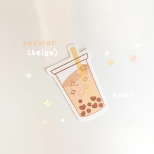 May include: A beige sticker with a cartoon illustration of a boba tea cup with brown boba pearls, a straw, and hearts and stars inside. The text "regular (beige)" and "nom!" are also on the sticker.