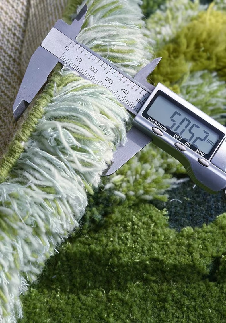 May include: Close-up of a green and white rug fringe being measured with a digital caliper. The caliper reads 5.063 mm.