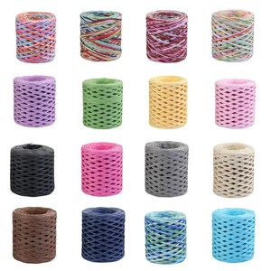 Puede incluir: Dieciséis carretes cilíndricos de cinta de rafia dispuestos en una cuadrícula de cuatro por cuatro. Los carretes presentan varios colores sólidos, incluyendo negro, marrón, rosa, amarillo, verde, azul y morado, junto con varias opciones multicolores, rayadas y jaspeadas.