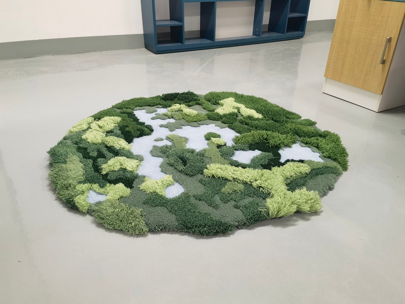 May include: A green and white rug with a textured, landscape design. The rug is made of soft, fluffy material and resembles a miniature forest.