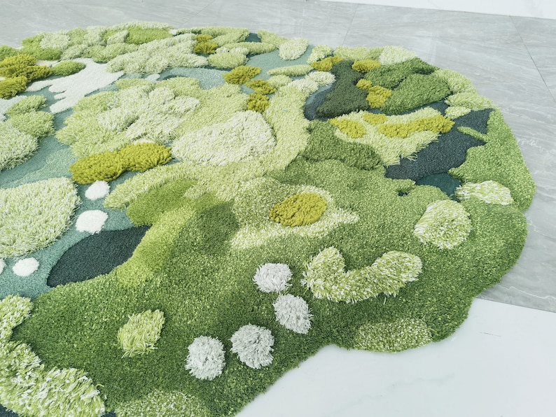 May include: A green, white, and yellow abstract rug with a fluffy texture. The rug has a unique, organic shape and is made of soft, plush fibers.