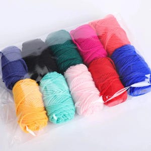May include: A clear plastic bag containing twelve individual skeins of yarn in various solid colors including yellow, teal, light pink, red, blue, dark green, black, purple, magenta, and orange, arranged in a grid pattern for storage.