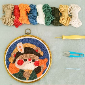 May include: A punch needle embroidery kit with a cartoon character design. The kit includes various coloured yarn skeins, a punch needle tool, scissors, and a needle. The embroidery hoop is approximately 15 cm in diameter.