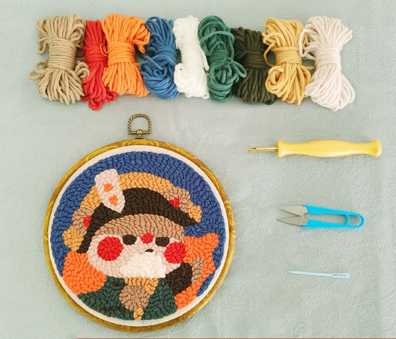 May include: A punch needle embroidery kit with a cartoon character design. The kit includes various coloured yarn skeins, a punch needle tool, scissors, and a needle. The embroidery hoop is approximately 15 cm in diameter.