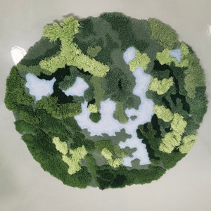 May include: A round, green and white rug with a camouflage pattern. The rug is made of fluffy, textured yarn.