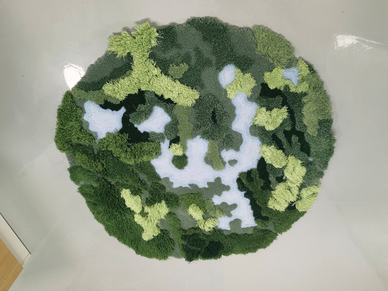 May include: A round, green and white rug with a camouflage pattern. The rug is made of fluffy, textured yarn.