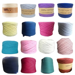 May include: A collection of sixteen cylindrical spools of yarn in various solid colors including cream, light blue, purple, dark blue, yellow, pink, white, turquoise, and red. Some spools feature brown paper labels with the text 100% Cotton.