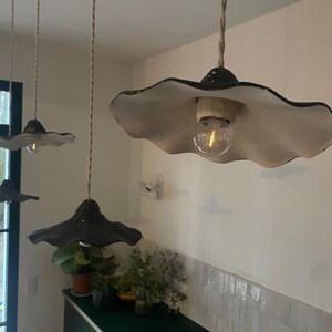 May include: Three pendant lights with a unique design. Each light features a black, scalloped shade with a white interior, suspended from a twisted cord. The exposed light bulbs emit a warm glow, adding a decorative touch to the room.