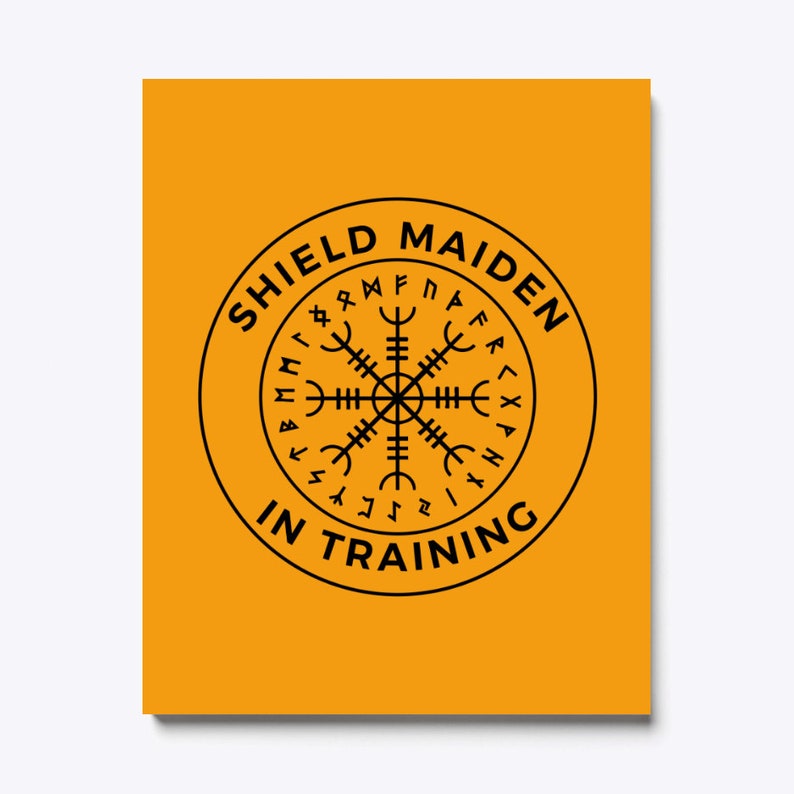 以下が含まれることがあります： 黄色の背景に、黒い円の中に「Shield Maiden in Training」という文字と、周囲にルーンが描かれた黒いコンパスが描かれています。
