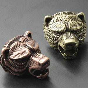 May include: Three bear head rings in different metal finishes: gold, silver, and copper. The rings are detailed with textured fur and sharp teeth.