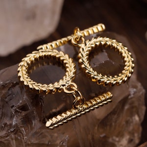 May include: Gold-toned jewellery with a leaf-like design. The jewellery features two connected rings and a clasp.