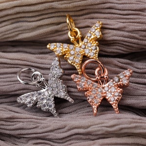 Può includere: Tre ciondoli a forma di farfalla in oro, argento e oro rosa con accenti di cristallo trasparente. I ciondoli sono su uno sfondo di tessuto morbido marrone.