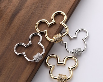 Puede incluir: Tres abalorios de Mickey Mouse en forma de Mickey Mouse de oro y plata con una banda incrustada de cristales transparentes. Los abalorios están sobre una superficie de madera.