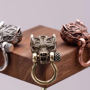 Puede incluir: Tres llaveros con cabeza de lobo en acabados plateado, latón y cobre. Cada llavero presenta un diseño detallado de cabeza de lobo con un anillo adjunto.