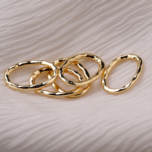 May include: Five gold-toned oval rings, stacked and overlapping, with a hammered or textured finish. The rings are on a white fabric background.
