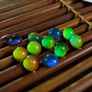 May include: A collection of iridescent glass marbles in shades of green, blue, and yellow. The marbles are arranged on a wooden surface.