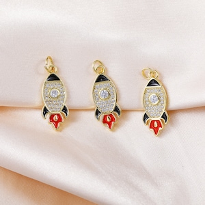Può includere: Tre ciondoli a forma di razzo dorati con accenti in smalto nero e rosso e strass trasparenti.