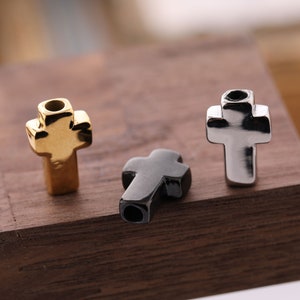 May include: Three metal cross charms in gold, silver, and black.