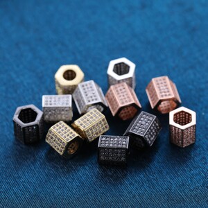 May include: Assortment of hexagonal-shaped beads with a pave setting of clear cubic zirconia stones. The beads are in various metal finishes, including silver, gold, rose gold, and black.