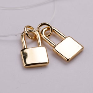 Puede incluir: Dos dijes de candado de color dorado que cuelgan de una cuerda transparente. Los candados son pequeños y tienen un diseño simple.