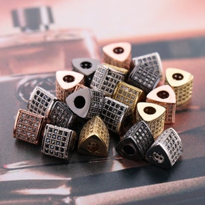 May include: A collection of triangular-shaped beads with a variety of finishes, including gold, silver, and rose gold. Each bead is adorned with small, clear rhinestones.