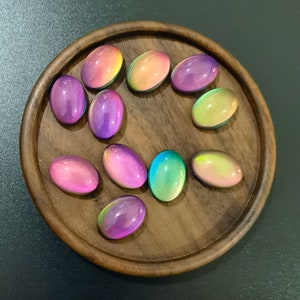May include: A collection of iridescent oval-shaped stones in various shades of pink, purple, green, and yellow, arranged on a wooden surface.