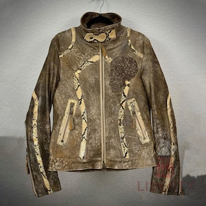 May include: Brown leather jacket with snake skin detailing and a skull motif. The jacket has a high collar, zip closure, and pockets. Sleeves feature zip details. The jacket is hanging on a black hanger.