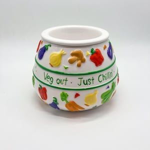May include: White ceramic pot with a wide opening, decorated with colorful vegetable designs. The pot features a green band with the text "Veg out. Just Chillin'". Vegetables include red peppers, eggplants, carrots, and onions.