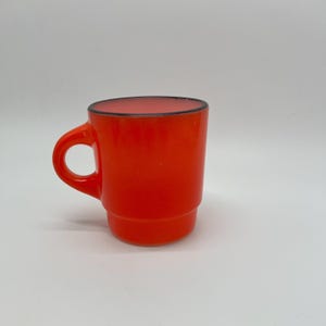 May include: A vibrant orange mug with a black rim and a rounded handle. The mug has a stacked design and is set against a plain white background. This mug is perfect for coffee, tea, or any hot beverage.