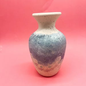 May include: A small, decorative ceramic vase with a light blue and pink speckled glaze. The vase has a rounded body and a slightly flared opening.