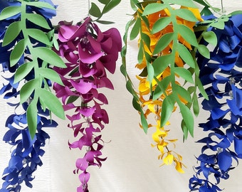 Può includere: Tre fili di fiori di carta appesi al soffitto. I fiori sono blu, viola e gialli. I fiori sono fatti di carta e hanno la forma di glicine.