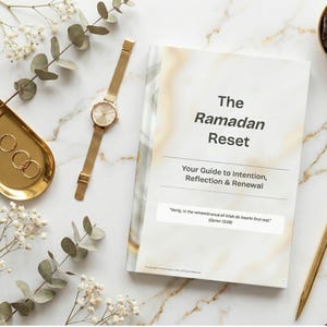 May include: A flat lay featuring a book titled "The Ramadan Reset" with gold accents. A gold watch, pen, and jewelry tray are arranged around the book. Dates in a gold bowl and a string of prayer beads complete the scene.