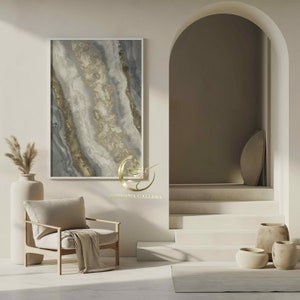 Pu&ograve; includere: Una stanza bianca con una poltrona beige, un vaso con erba della pampa secca e un dipinto astratto incorniciato in tonalit&agrave; dorate e grigie. La stanza presenta anche una scala bianca con un arco arrotondato che conduce a un corridoio. Il testo "NIRVANA GALLEKT" &egrave; visibile nella parte inferiore centrale dell'immagine.
