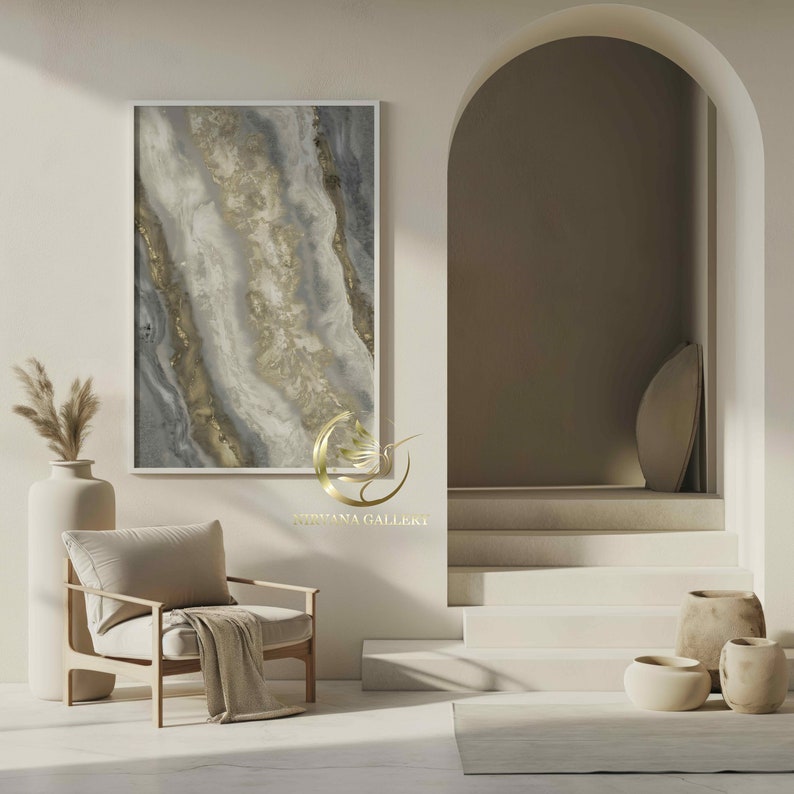 Pu&ograve; includere: Una stanza bianca con una poltrona beige, un vaso con erba della pampa secca e un dipinto astratto incorniciato in tonalit&agrave; dorate e grigie. La stanza presenta anche una scala bianca con un arco arrotondato che conduce a un corridoio. Il testo "NIRVANA GALLEKT" &egrave; visibile nella parte inferiore centrale dell'immagine.
