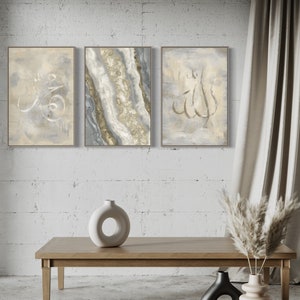 Pu&ograve; includere: Tre dipinti astratti incorniciati con calligrafia araba in oro e bianco su uno sfondo grigio chiaro. I dipinti sono appesi a un muro di mattoni bianchi. Un tavolino da caff&egrave; in legno con un vaso in ceramica bianca e altri due vasi in nero e beige sono in primo piano.
